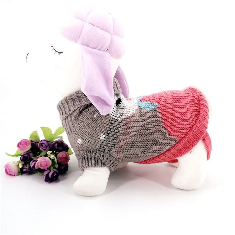 A plush white dog toy wearing a festive knit pet sweater with gray pink and blue sections featuring snowflake winter dog apparel.