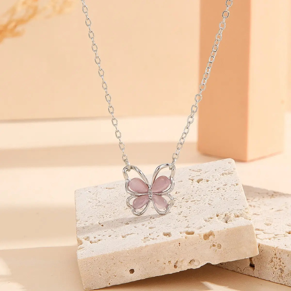 Un delicado collar con dije de mariposa de plata, con alas de gema rosa translúcidas, presenta el diseño del collar con dije de mariposa de gema translúcida.