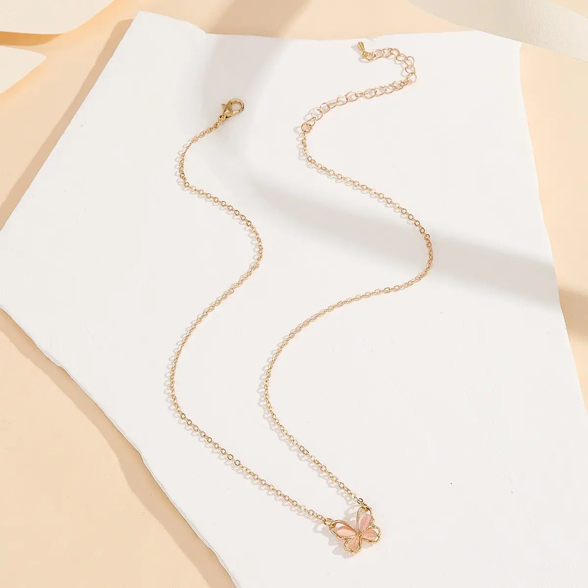 Un delicado collar de cadena con baño de oro, con un pequeño dije de mariposa de esmalte rosa en un diseño de collar con dije de mariposa de gema translúcida.