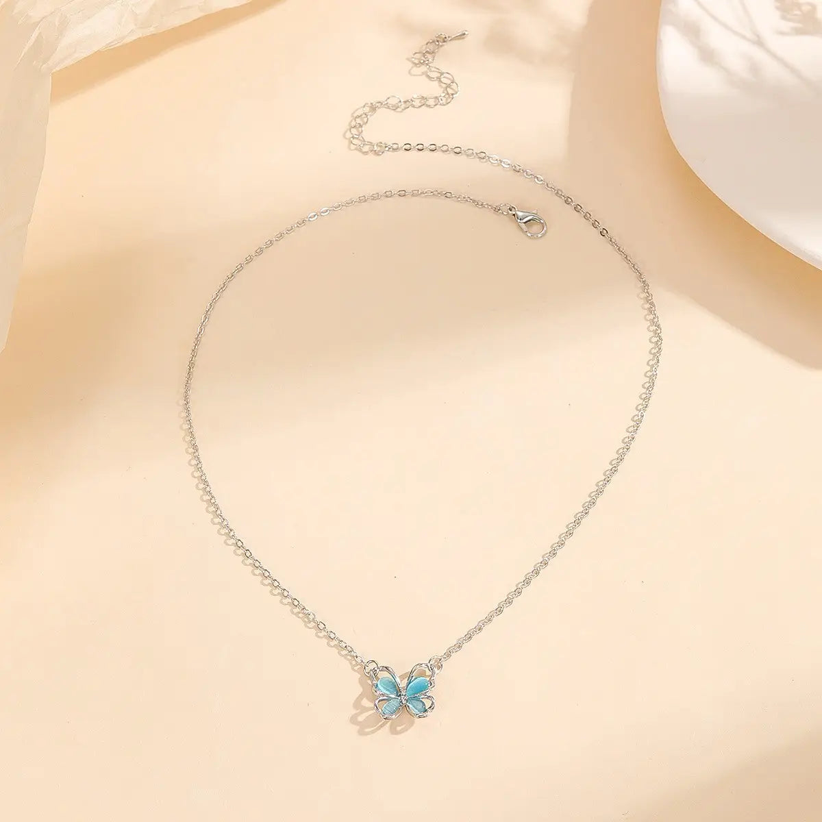 Un collar de cadena de plata con un delicado dije de mariposa, con alas de esmalte azul claro en un diseño de collar con dije de mariposa de gema translúcida.