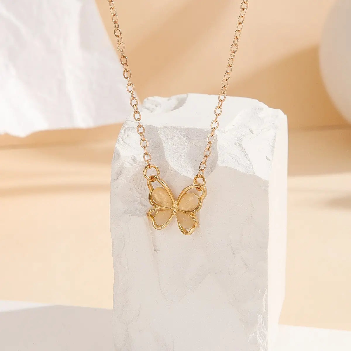 Un collar de mariposa con baño de oro, con alas de gema color durazno translúcido en un diseño de collar con dije de mariposa de gema translúcida.