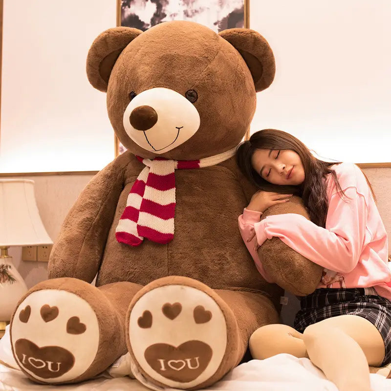Ein brauner riesiger Plüsch-Teddybär-Plüsch mit weißem Schnäuzchen, schwarzen Knopfaugen und einem rot-weiß gestreiften Schal um den Hals.