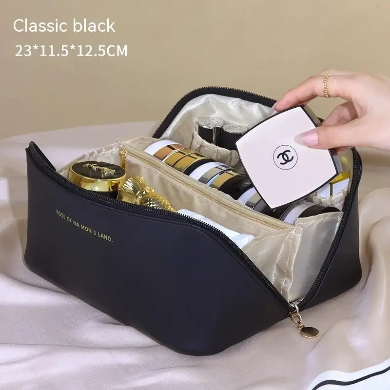 Klassische schwarze Reisekosmetiktasche aus PU-Leder mit großem goldfarbenem Reißverschluss und Innenfutter mit dem Text „rose of na mons land“ seitlich platziert.