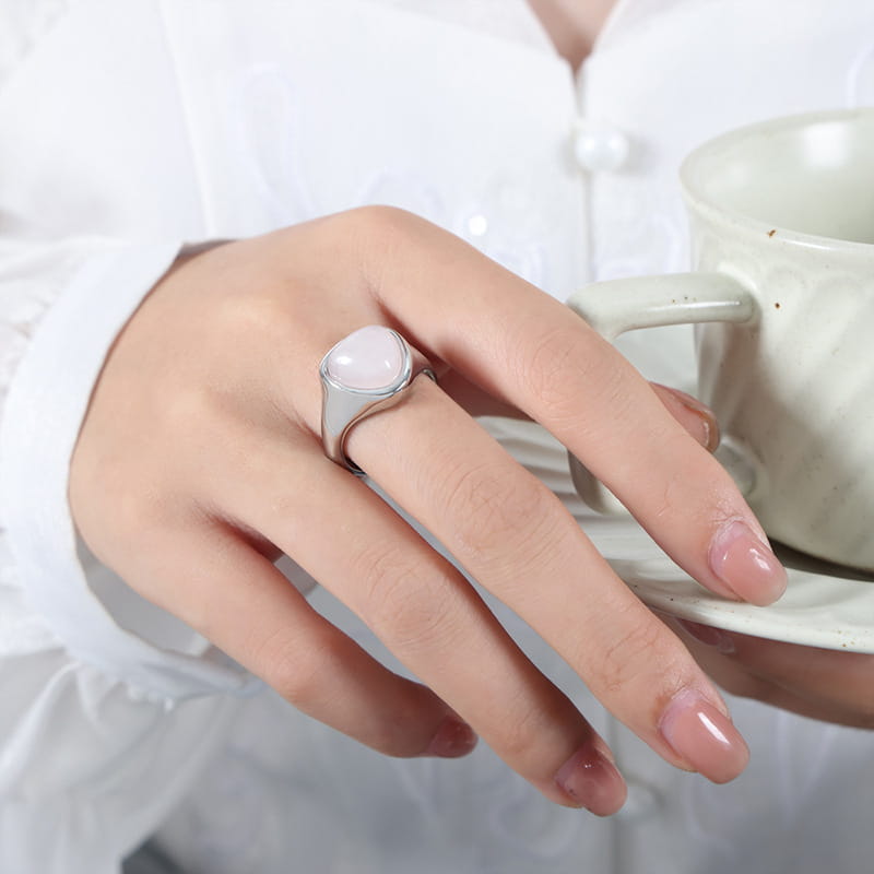 A sleek silver heart shaped natural stone titanium steel signet ring featuring a smooth oval shaped pink stone set in a minimalist band.