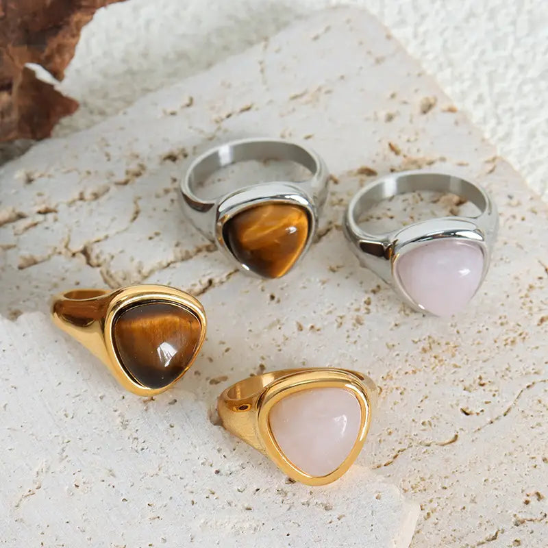 Set of four statement heart shaped natural stone titanium steel signet rings featuring triangular tiger eye and rose quartz stones in gold and silver toned metal settings.