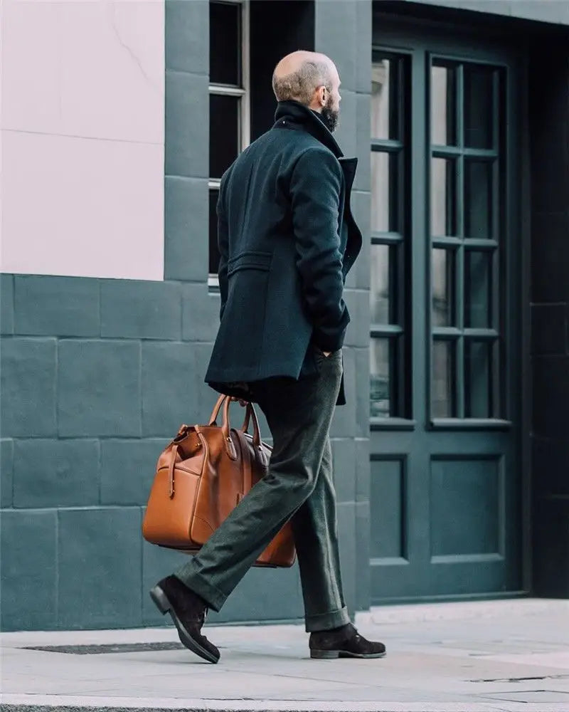 brown leather briefcase with top handles and a structured rectangular design paired with an olive green wool double-breasted coat.