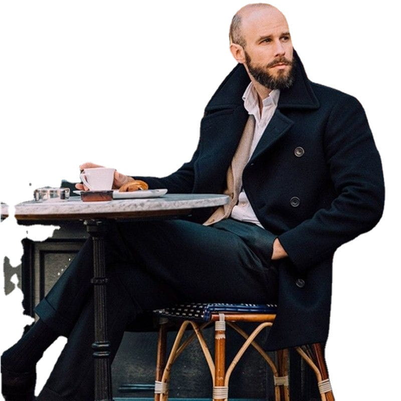 A man seated at an outdoor café table wearing a dark navy double-breasted wool overcoat with notched lapels and black buttons featured in an olive green wool double-breasted coat product.