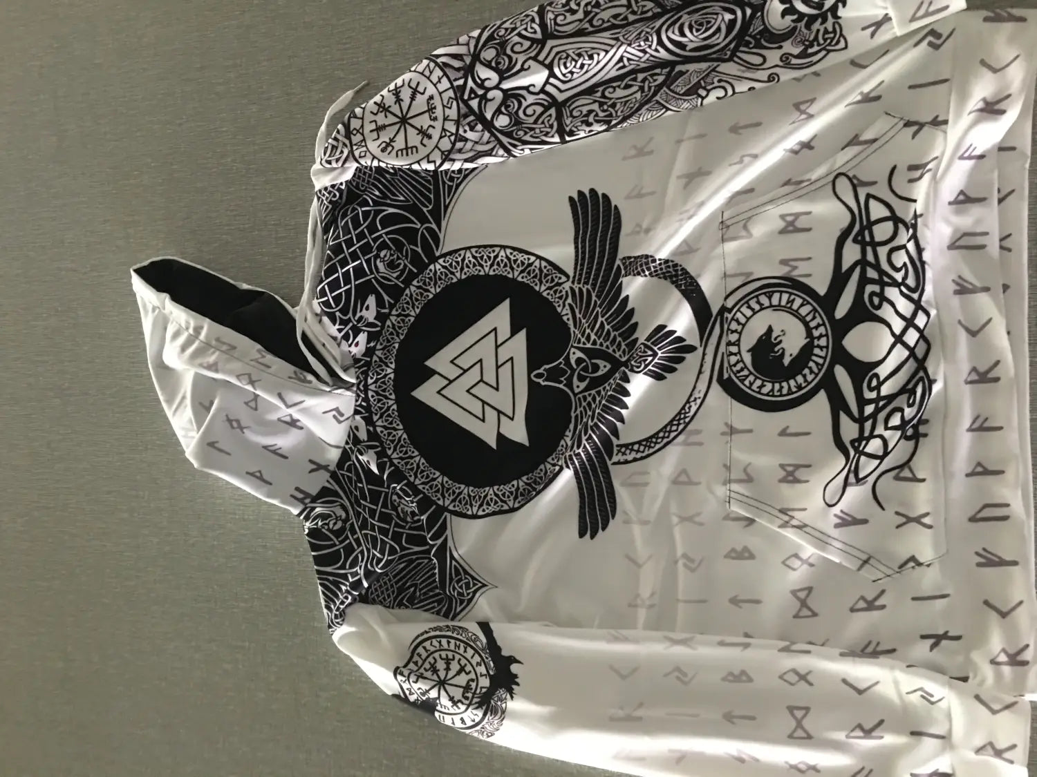 White hooded sweatshirt featuring intricate black Norse-inspired 3D print designs including a central Valknut symbol surrounded by an eagle and runes.