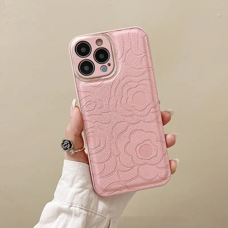 The back side of a pink camellia leather phone case for iPhone 11 to 14 with a floral-patterned embossed textured design.