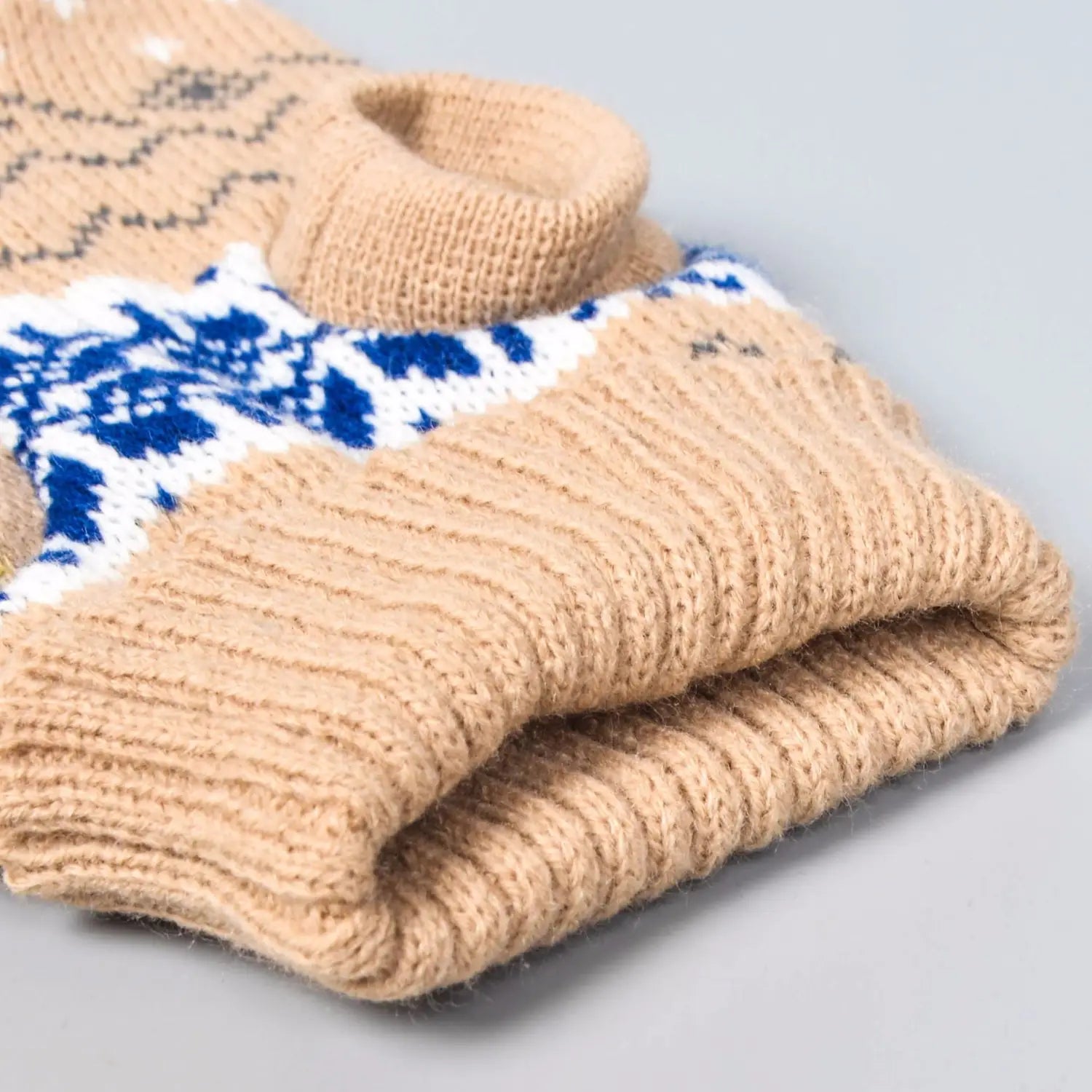 A beige knitted dog sweater with a ribbed texture and a blue and white nordic snowflake pattern for winter pet apparel.