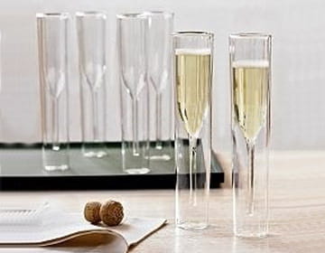Deux flûtes à champagne transparentes à double paroi remplies d’un liquide doré pétillant sur une surface en bois, à côté de bouchons de vin fermés par liège et d’un livre ouvert, dans un ensemble de flûte à champagne en verre à double paroi de 115 ml.