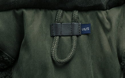 Tela de chaqueta de invierno acolchada con forro polar para tallas grandes color verde oscuro con etiqueta de cuero negro que muestra la talla us slash s en texto blanco.