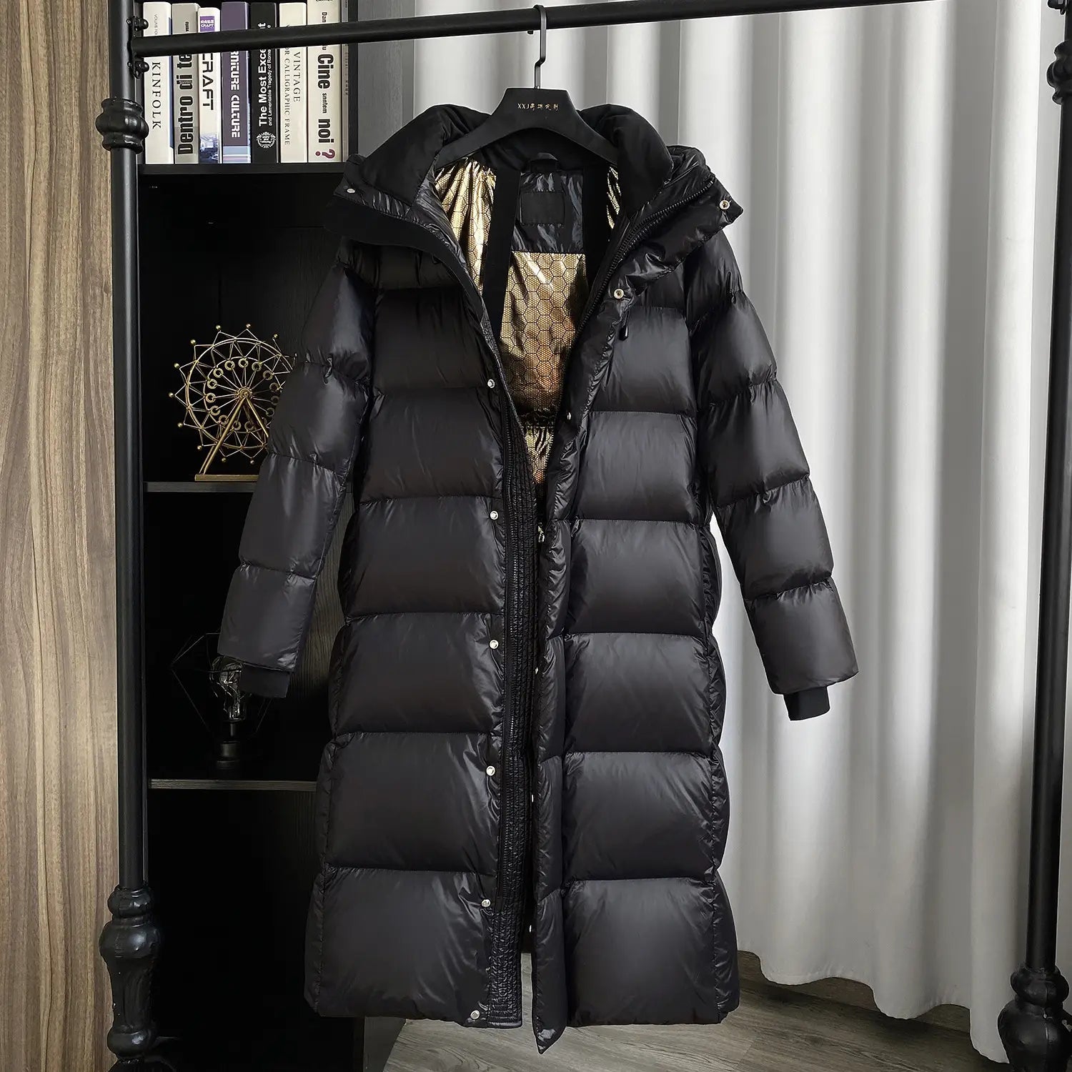 Black down jacket hooded quilted puffer coat in black with a quilted design and shiny silver buttons hanging on a hanger.