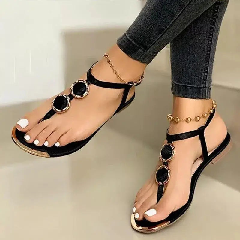 Black thong flat sandals with beaded ankle straps gold-toned circular metal embellishments and a metallic heel for women.