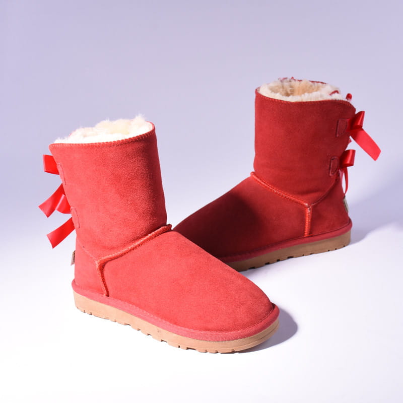 women snow boots showing the back side in red suede with a fluffy white fur interior and red ribbon bow ties designed for winter warmth and style.