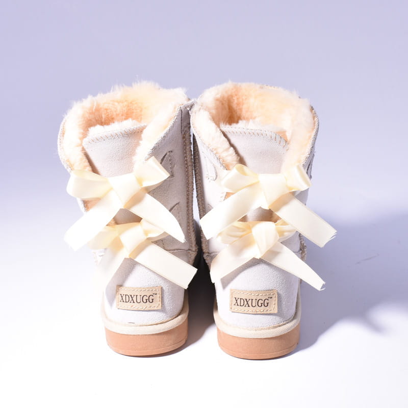 Cream-colored suede women snow boots with warm fluffy shearling lining and decorative bows at the ankle designed for winter wear.