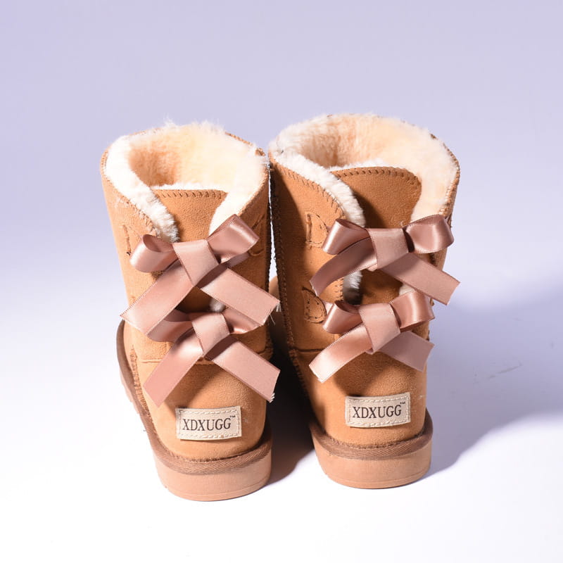 Tan ugg-style women snow boots with warm suede, plush white fur lining, and matching satin bows tied across the front for winter wear.