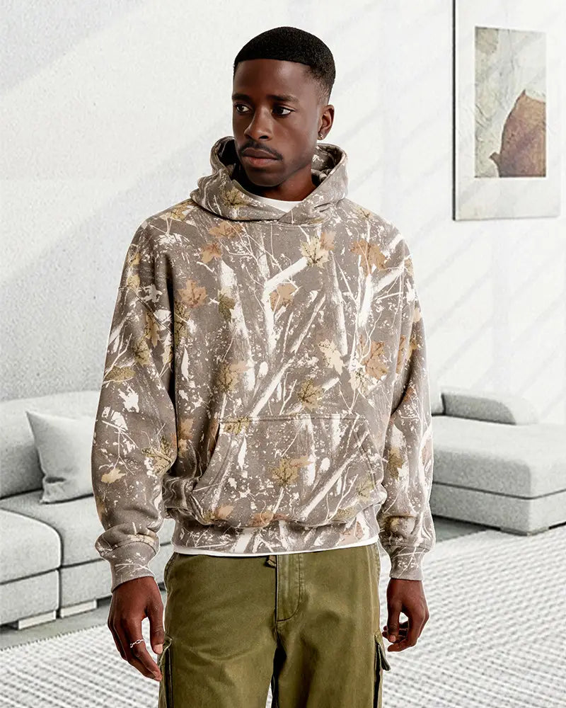 Un sweat à capuche surdimensionné unisexe rétro en tricotage tie-dye 3D, avec un motif camouflage délavé olive et beige, une coupe décontractée, des motifs discrets de feuilles et des poignets côtelés.