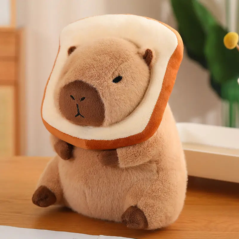 A plush capybara toy with a soft beige body and brown nose wearing a bread-shaped hood made from white and golden-brown fabric from the capybara plush toy with bread and flower outfits collection.