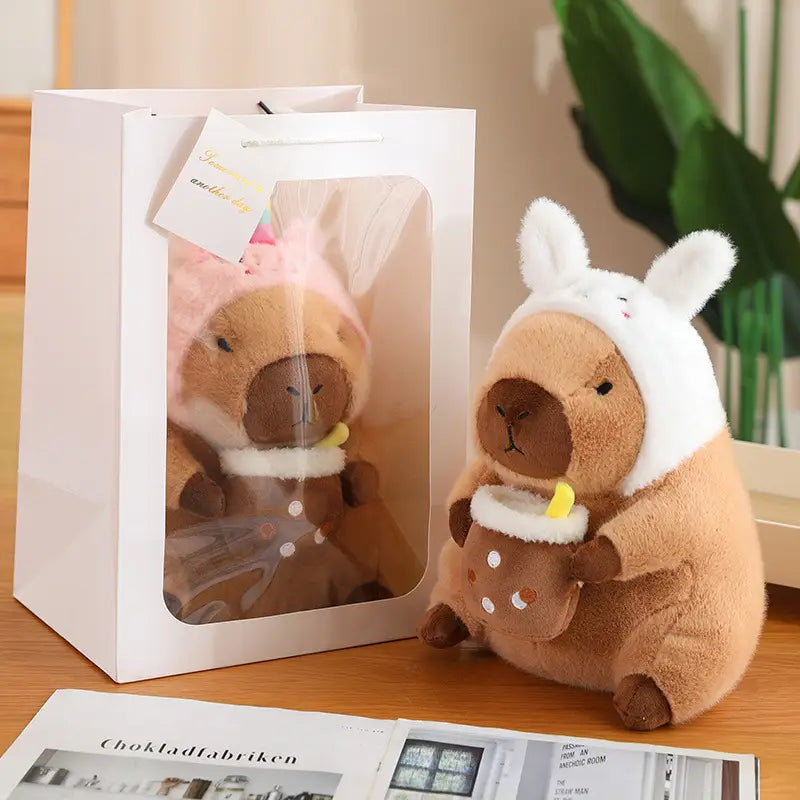 a plush capybara toy wearing a white bunny hat and holding a small brown polka dot cup featured in bread and flower outfits collection