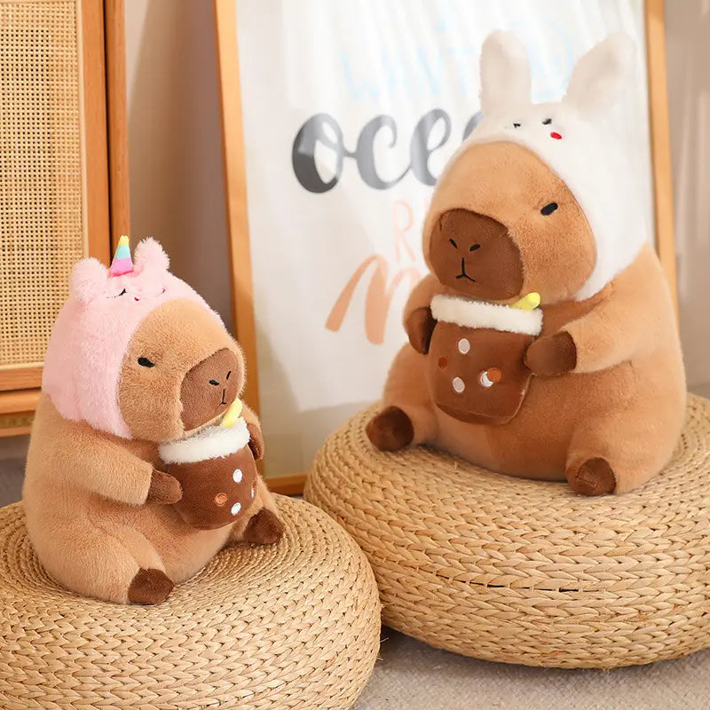 soft brown plush capybara stuffed animals wearing cozy hooded outfits with a pink unicorn horn and white bunny ears in bread and flower themed designs