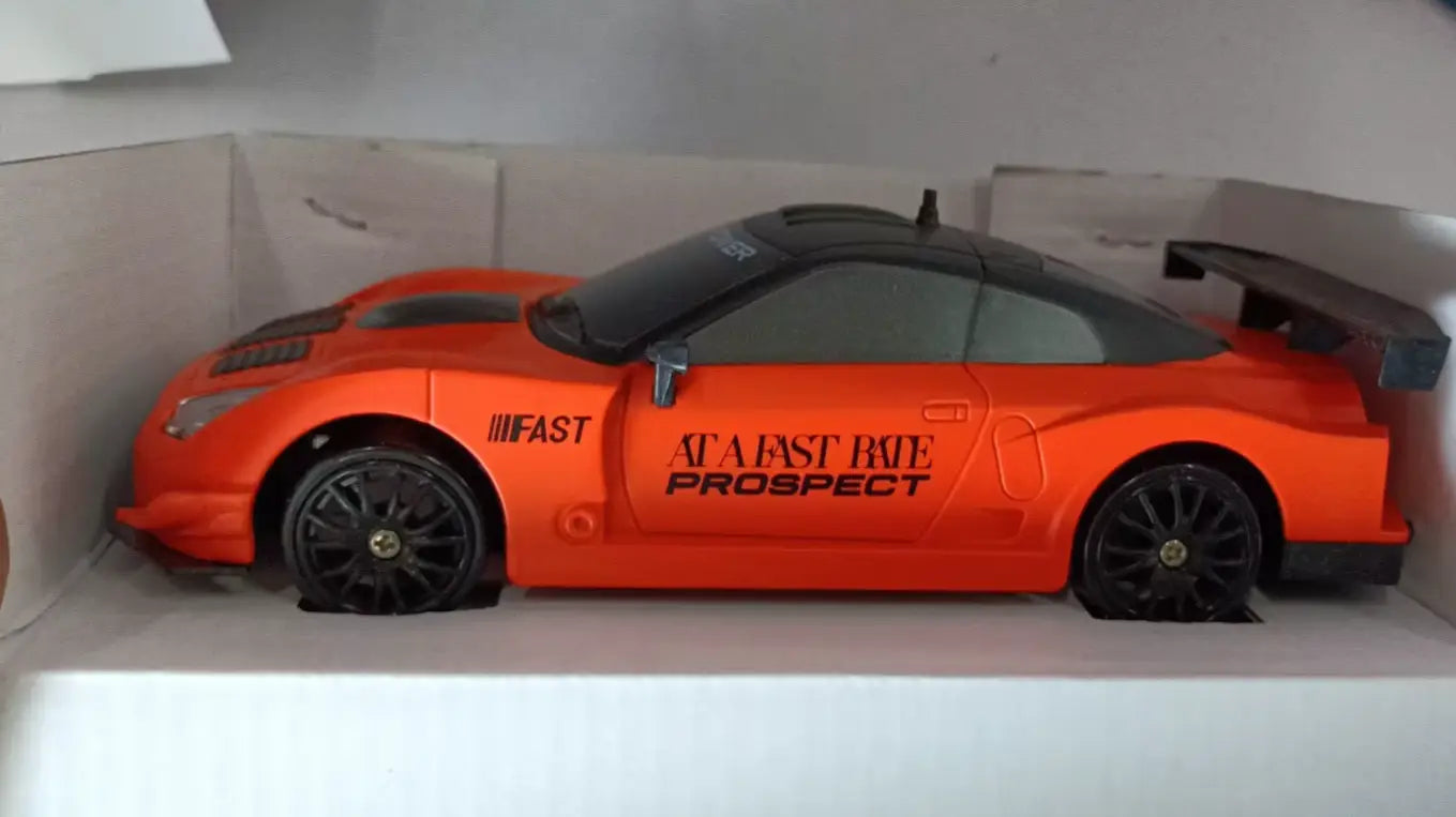 Voiture de drift RC orange avec toit noir, roues et aileron, avec des autocollants de conduite rapide et une perspective de trajet rapide, conçus comme un jouet de GTR télécommandé 4WD à haute vitesse.