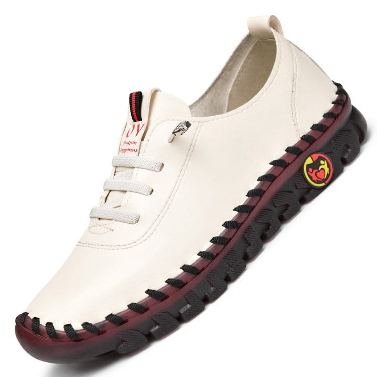 Cremefarbener handgefertigter PU-Lederschuh im Slip-On-Design mit flacher, lässiger Passform, mit schwarzer Naht entlang der Sohle und einem roten sowie gelben runden Logo an der Seite.
