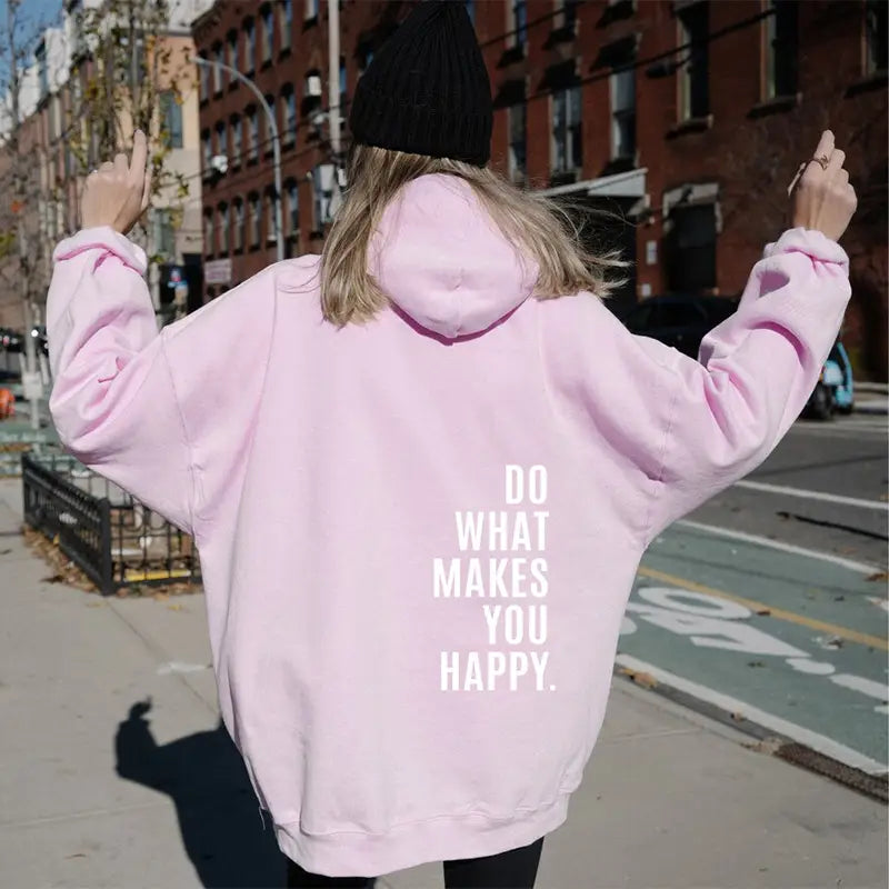 Sweat à capuche streetwear oversize rose fabriqué dans une matière douce, présentant du texte blanc « do what makes you happy » au dos.