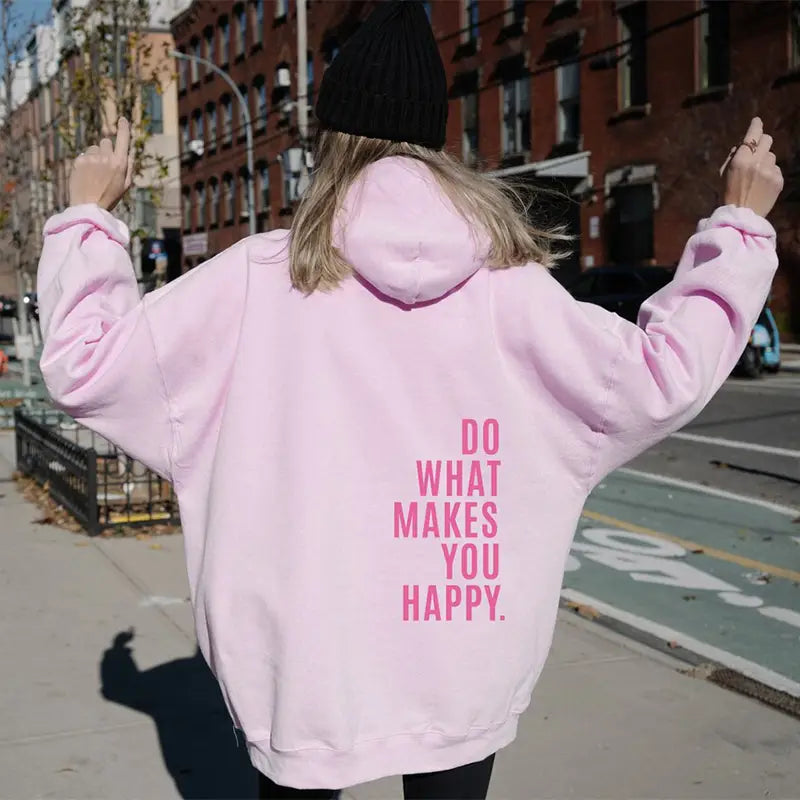 Le dos d’un sweat à capuche streetwear oversize rose doux présente un texte « do what makes you happy » verticalement, en caractères gras, dans une écriture rose vif.