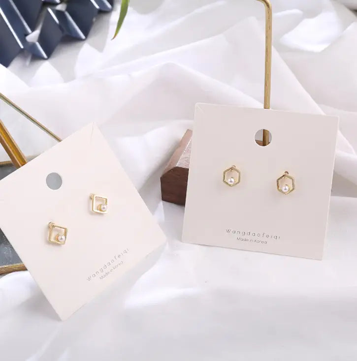 Goldfarbene Ohrstecker mit zarten geometrischen Pfeil- und hohlen Quadratfassungen mit einer einzelnen Perle in der Mitte.