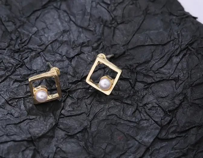 Goldene Ohrstecker mit eckigem Rahmen, jeweils mit einer mittig platzierten weißen Perle, mit geometrischem Pfeil- und hohlem Quadrendesign.