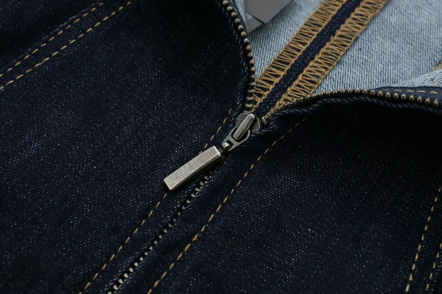 Détail de fermeture à glissière en denim bleu foncé avec tirette en métal à tons argentés et surpiqûres beige clair contrastantes sur une robe midi sans bretelles en denim à rayures fantaisie.
