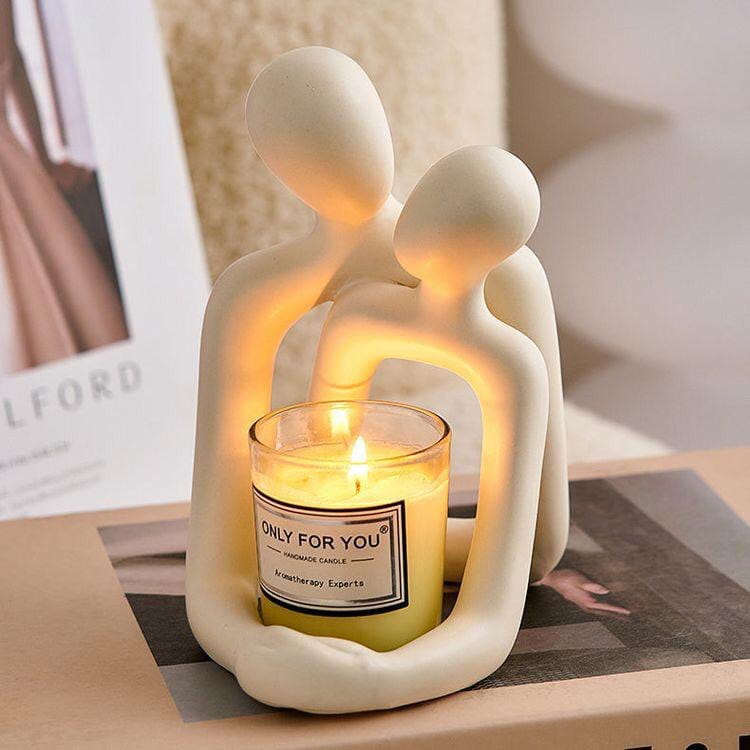 Elfenbeinfarbener Keramik-Kerzenhalter in Form von zwei abstrakt modellierten Figuren, die sich umarmen und eine beleuchtete gelb duftende Aromatherapie-Kerze in ihren Armen halten, aus der Kollektion abstrakter Keramik-Kerzenhalter mit Paar-Figuren aus Harz.