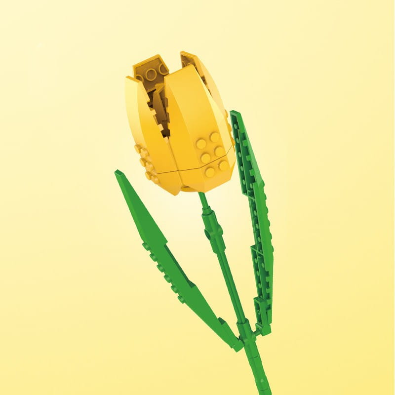 Un tulipe en Lego jaune avec une tige verte et des feuilles, réalisée en briques en plastique imbriquées, figurant dans un bouquet de fleurs en briques, rose bonsaï, jouet.