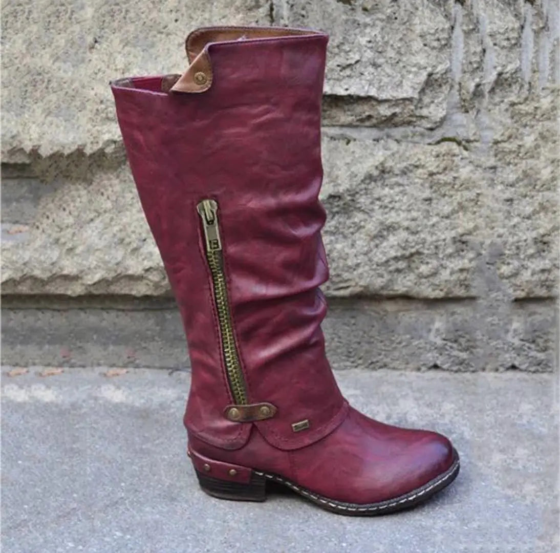 A maroon suede leather knee high boot with a block heel features a side zipper and brass colored hardware.
