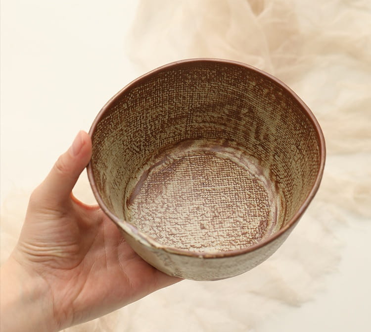 A hand holds a rustic brown ceramic rice bowl with a handcrafted textured speckled interior and exterior suitable for soup.