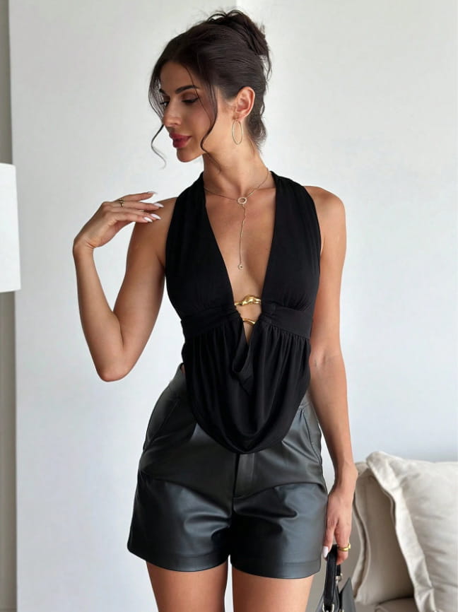 Black satin halter romper with a black halter neck top featuring a deep v cut and gold toned metallic belt detail at the waist with faux leather shorts.