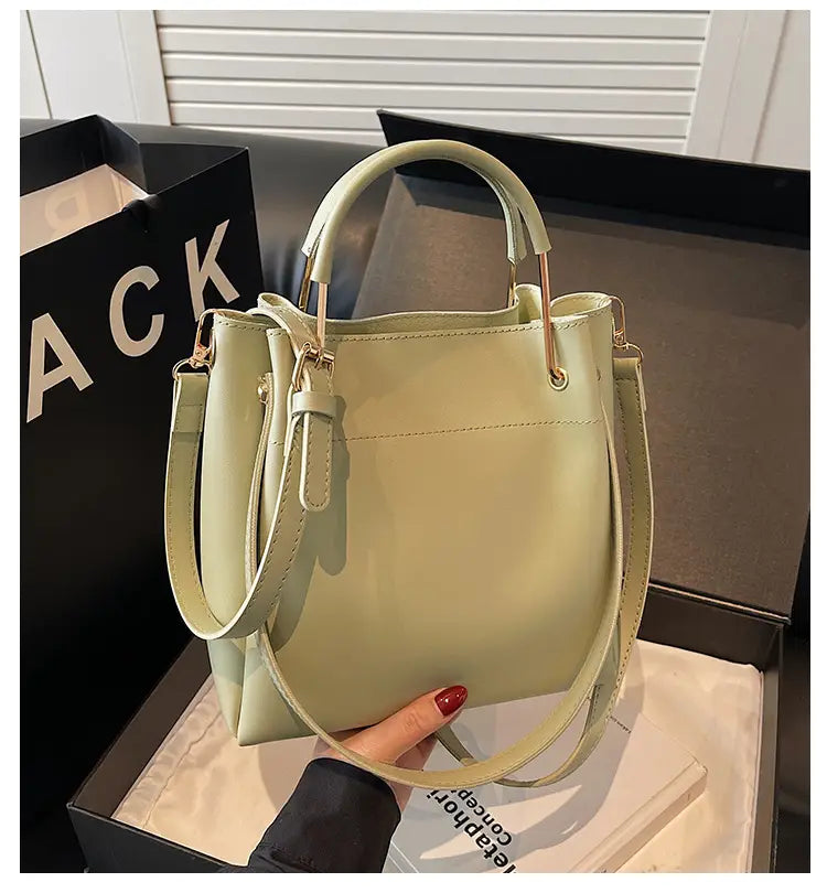 Minimalist leather bucket bag in pale green with a smooth matte finish and gold-tone hardware accents featuring a detachable strap.