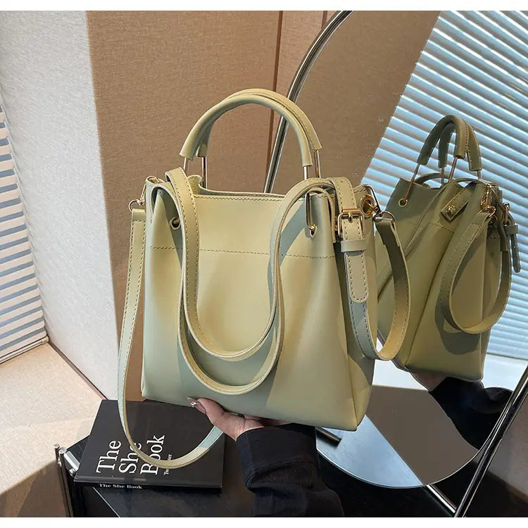 A minimalist leather bucket bag in pale green with dual top handles and a detachable shoulder strap.