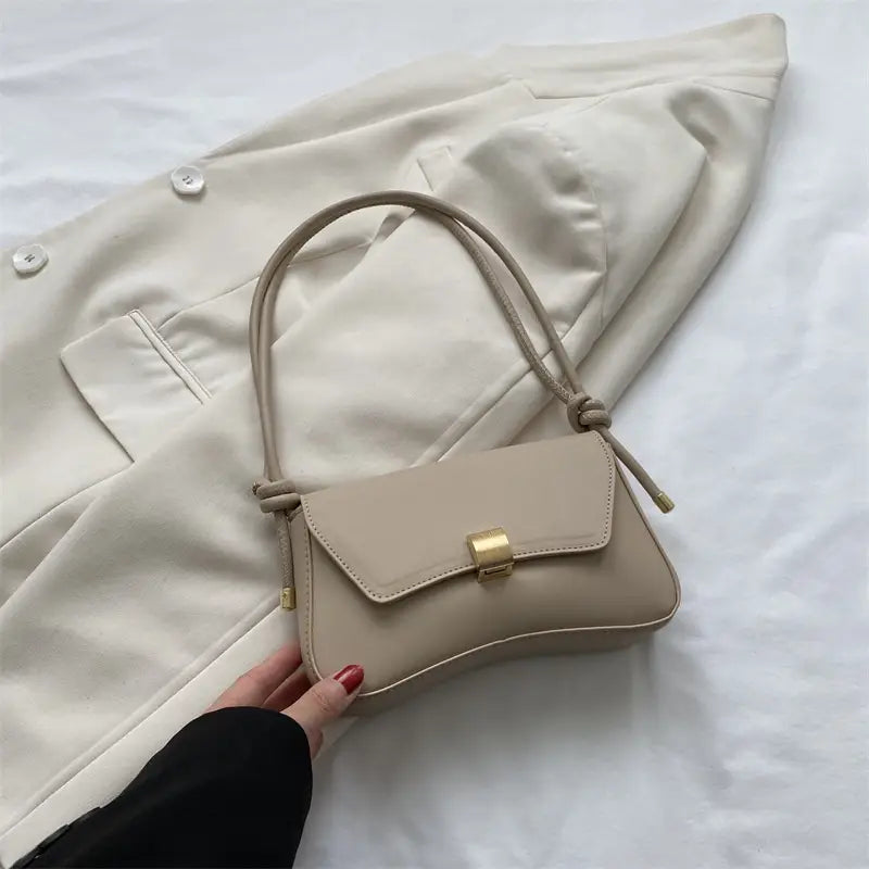 Beige minimalist faux leather structured shoulder bag with a gold-tone clasp and knotted strap.