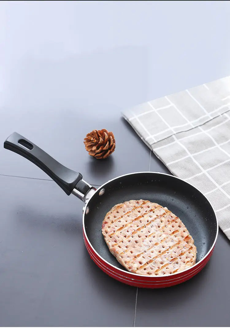 Red mini non-stick aluminum frying pan with black handle containing a golden-brown grilled pancake.