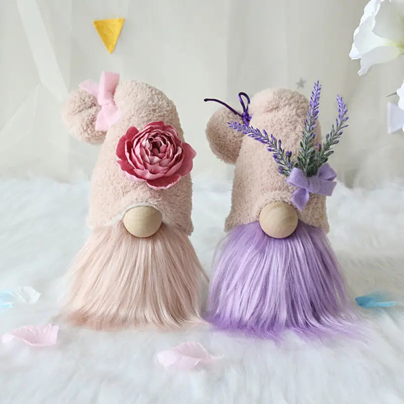 Two plush gnome dolls featuring soft beige fuzzy bodies, wooden nose pieces, long pastel faux-fur beards, one decorated with a pink rose and the other with lavender sprigs, designed as lavender and pink desktop ornaments.
