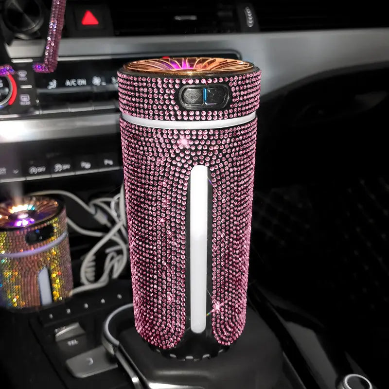 Ein mit rosa Strasssteinen verzierter Autoluftauffrischer mit einer goldfarbenen Oberseite und einem weißen vertikalen Streifen zur Verwendung als Diamant-Auto-Befeuchter-LED-Strass-USB-Luftdiffusor.