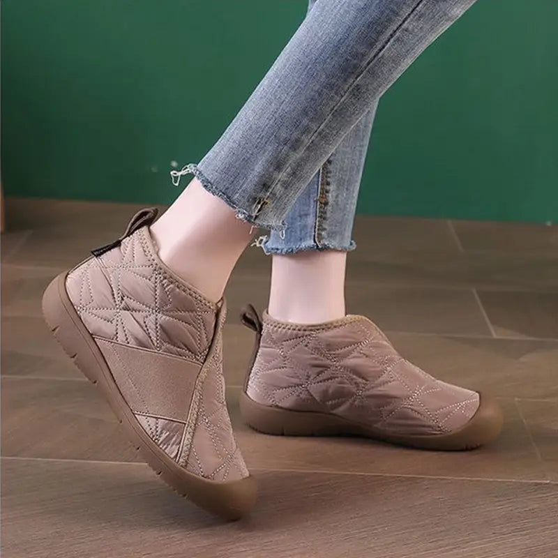 Cream-colored waterproof plush winter snow ankle boot with quilted design, brown rubber sole, and elastic side panel.