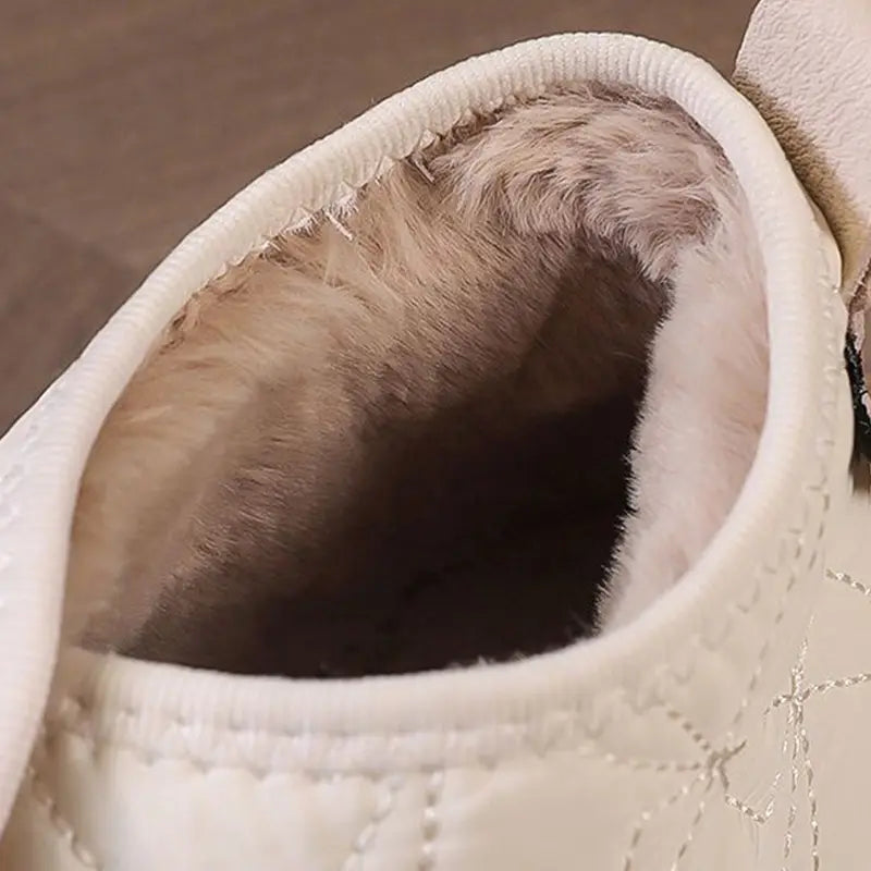 Cream-colored waterproof plush winter snow ankle boot with quilted design, brown rubber sole, and elastic side panel.