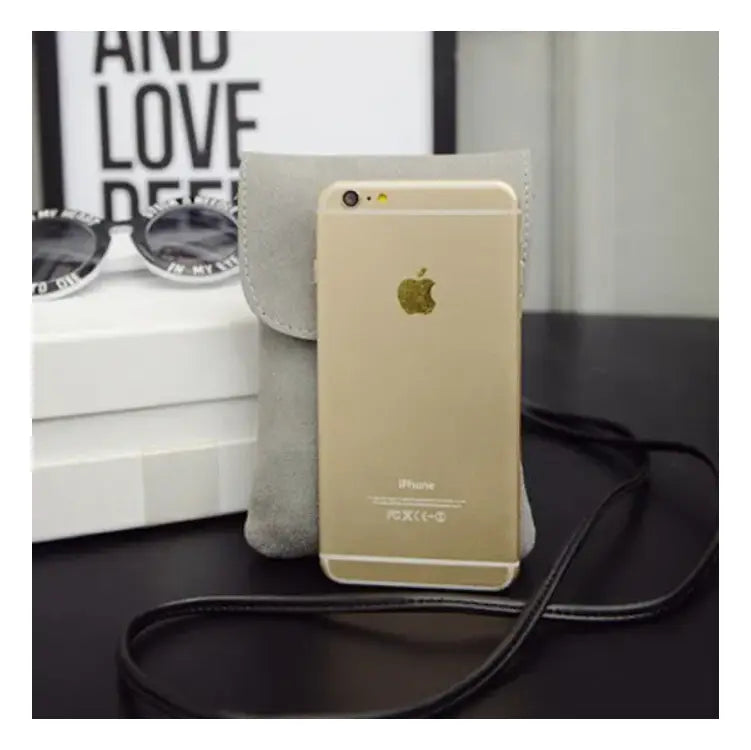a gold-colored iphone 6 with a black strap is displayed in front of an old worldly charm matte suede vegan leather crossbody bag in gray suede-like material