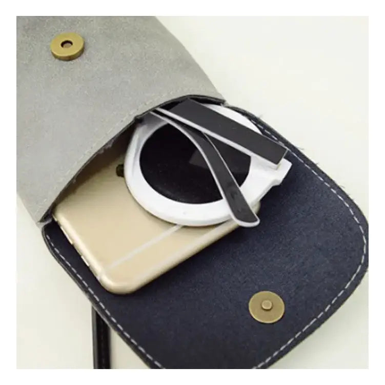 gray and navy felt phone case with brass-toned snap buttons holding a gold smartphone and white wireless charger beside the old worldly charm matte suede vegan leather crossbody bag