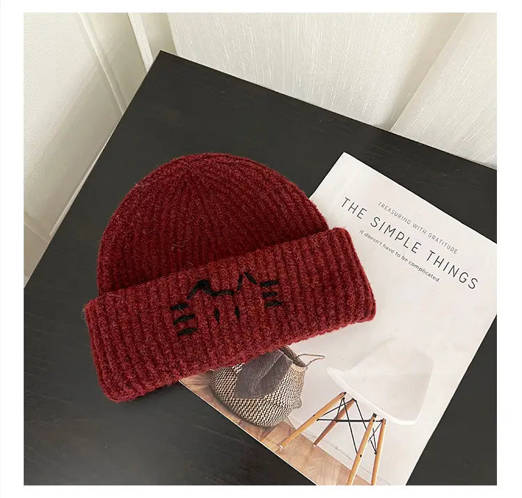 A cozy ribbed-knit maroon cat embroidered beanie hat with a folded brim featuring black mountain peaks.