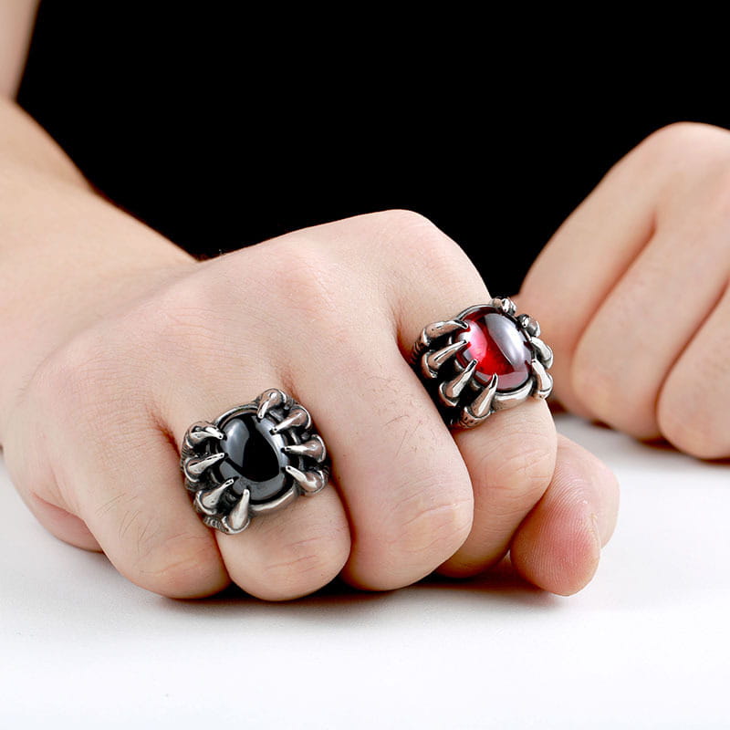 Two ornate dark-finished vintage titanium steel claw rings with black and red zircon gemstones worn on fingers.