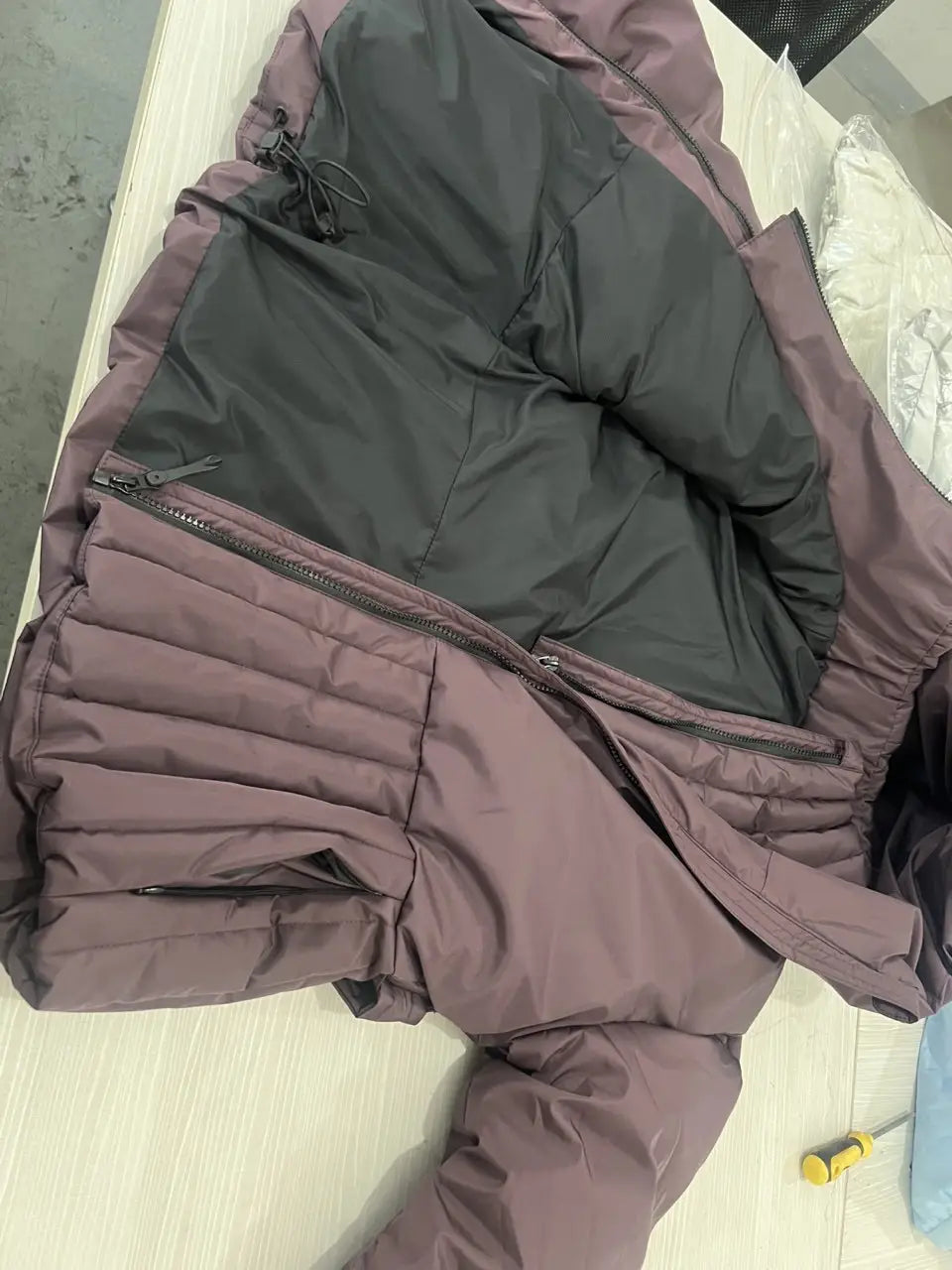 Women s belted hooded puffer coat in muted mauve quilted fabric with black lining featuring horizontal stitching and zipper details.